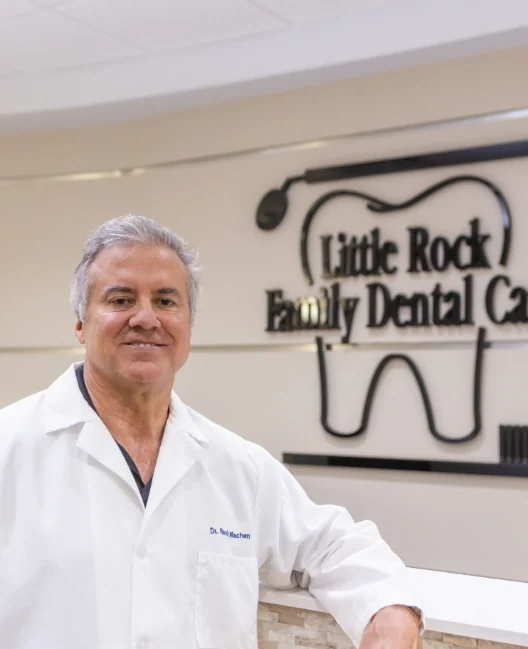 Dr. Randy Machen in his white coat at the reception desk, in front of the practice sign.